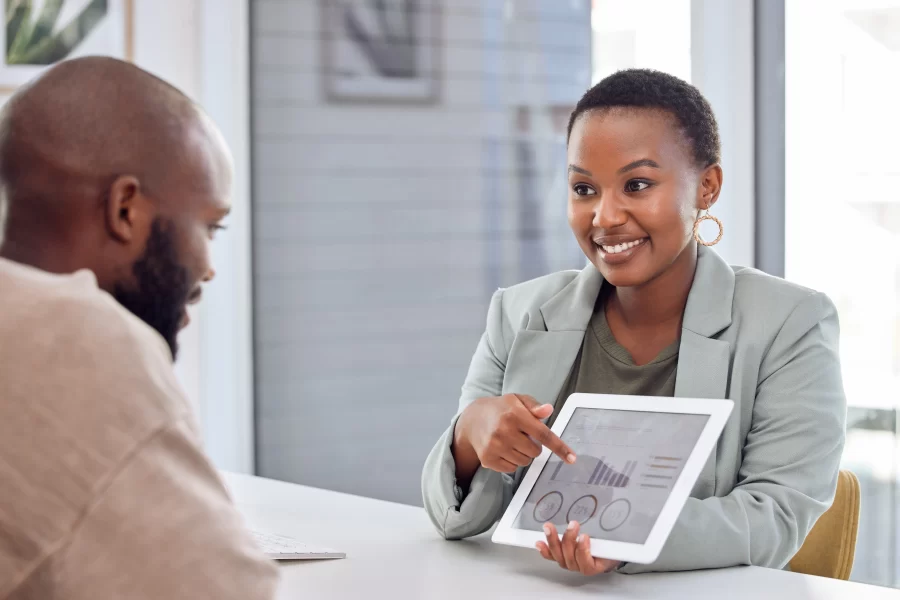 Short hair smiling lady showing analytics metrics to a gentleman on a table across her